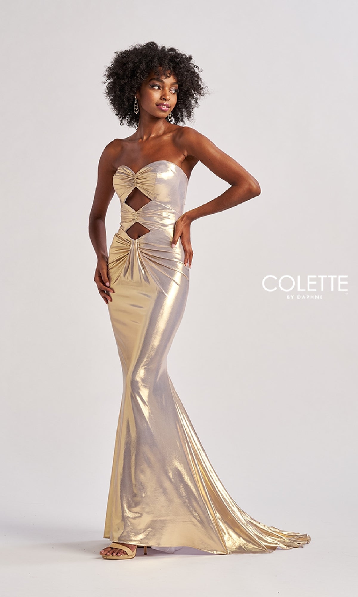 A woman poses against a white background in the Long Prom Dress: Colette CL8545—a strapless, metallic gold cut-out gown that is fitted, floor-length, and glamorous. The